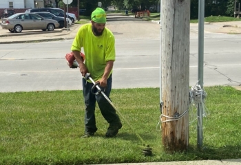 Man in yellow shirt operating a weedeater next to a sidewalk.