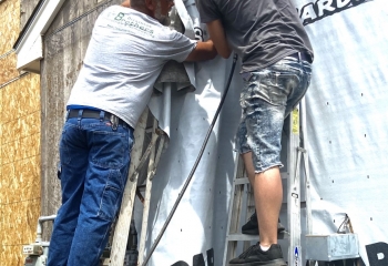 Two men attaching a plastic tarp on a building.